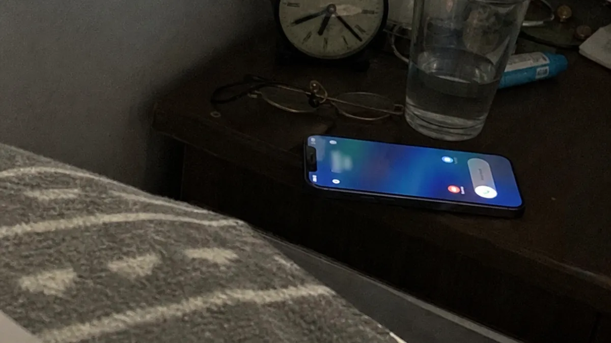 A smartphone on a nightstand glowing with an incoming call at 2 AM in a dark bedroom