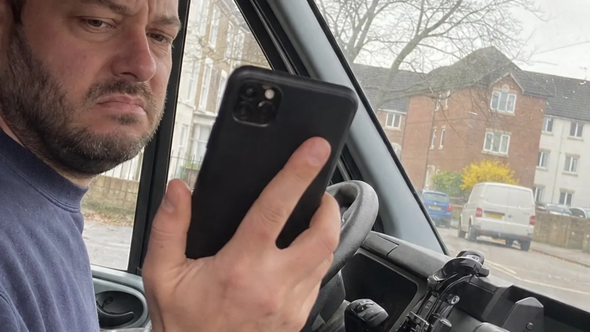 A frustrated plumber in his work van staring at his phone showing a robotic chat interface