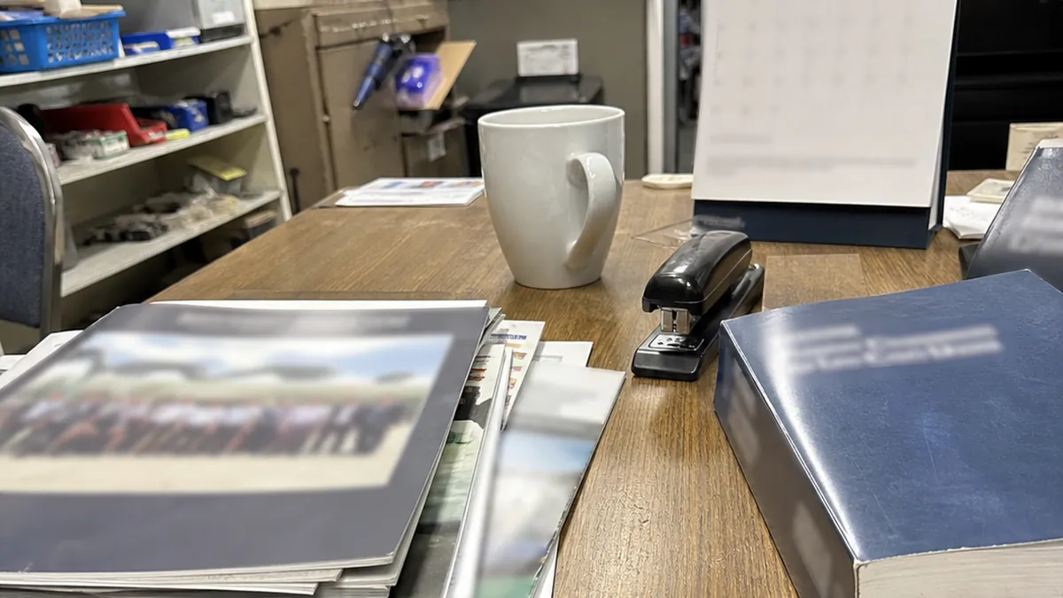 A stack of trade association newsletters and a plumbing code book on a shop office desk