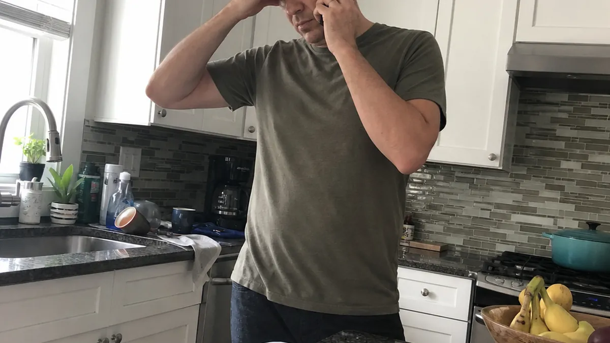A frustrated homeowner holding a phone away from her ear in a kitchen with a water leak