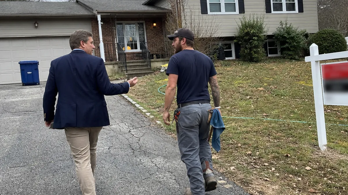 A real estate agent and a plumber shaking hands in front of a house with a for-sale sign