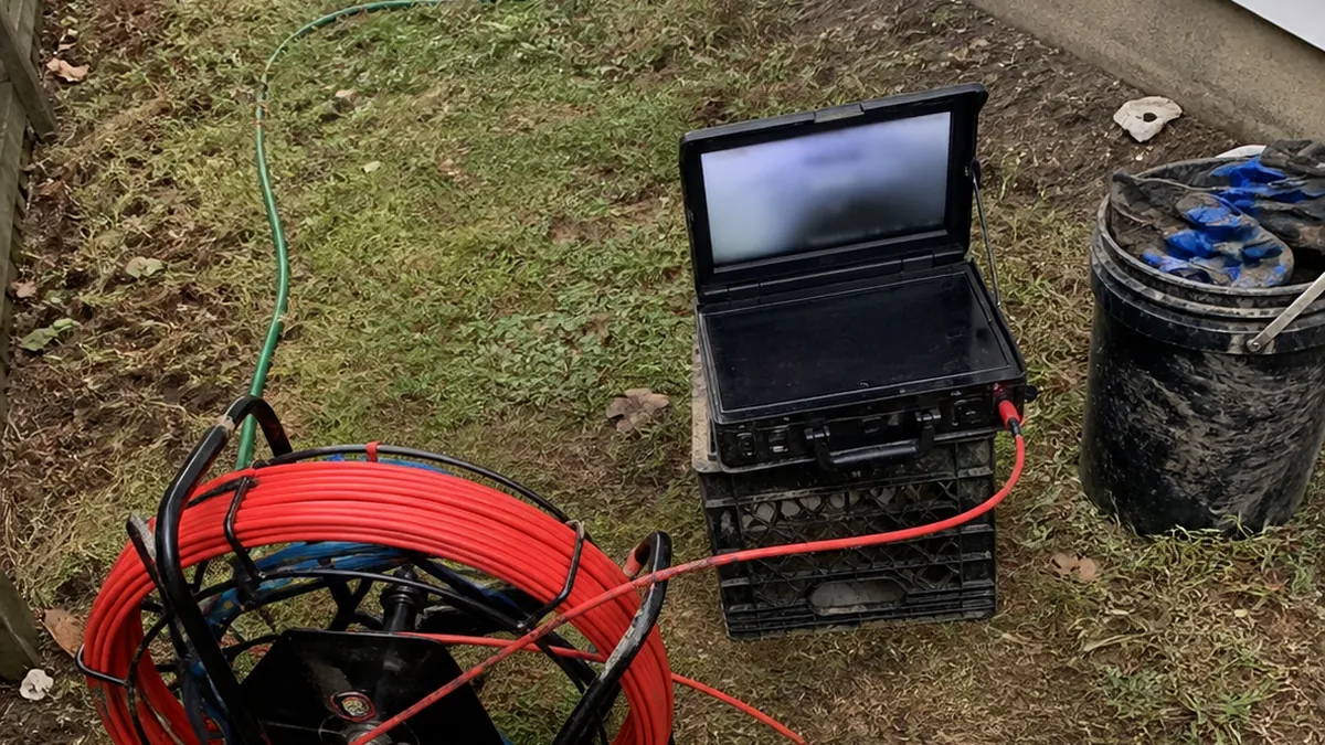 A sewer inspection camera reel and monitor set up next to a cleanout on a job site